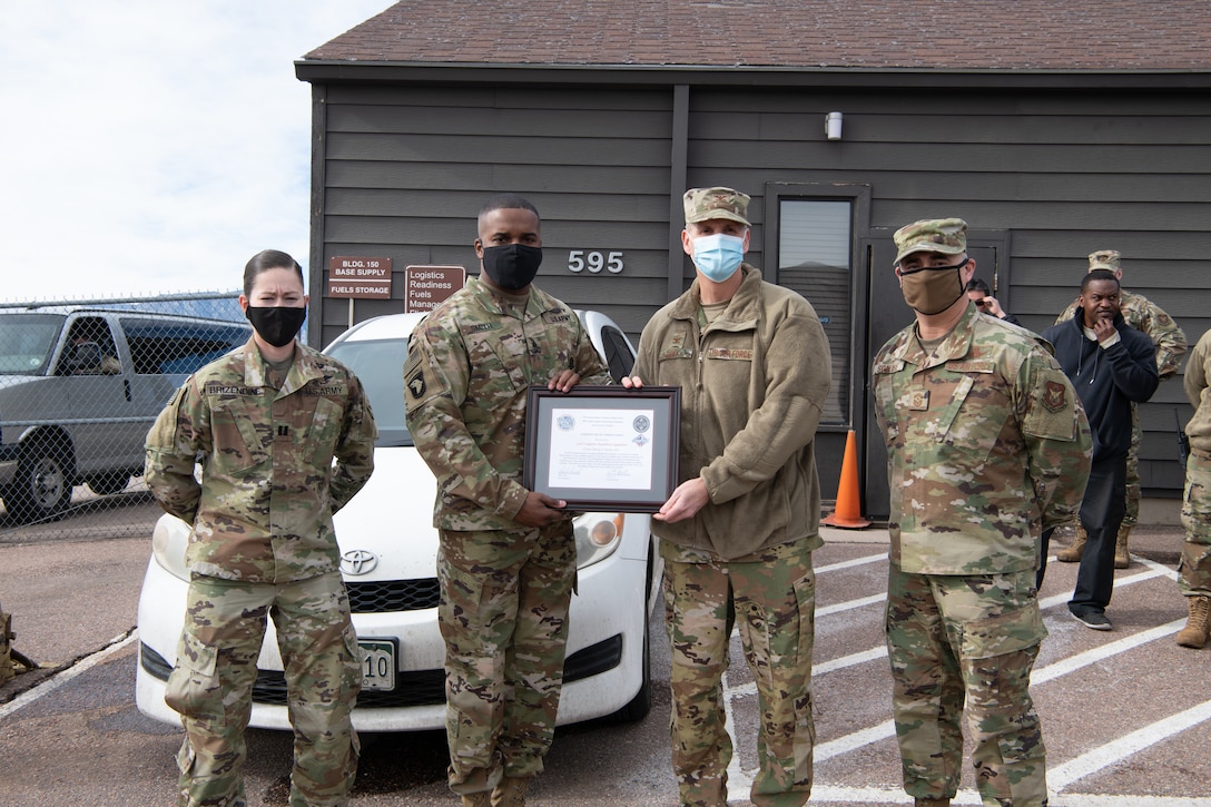 Two soldiers present a certificate of appreciation to two Airmen with a small audience in the background.