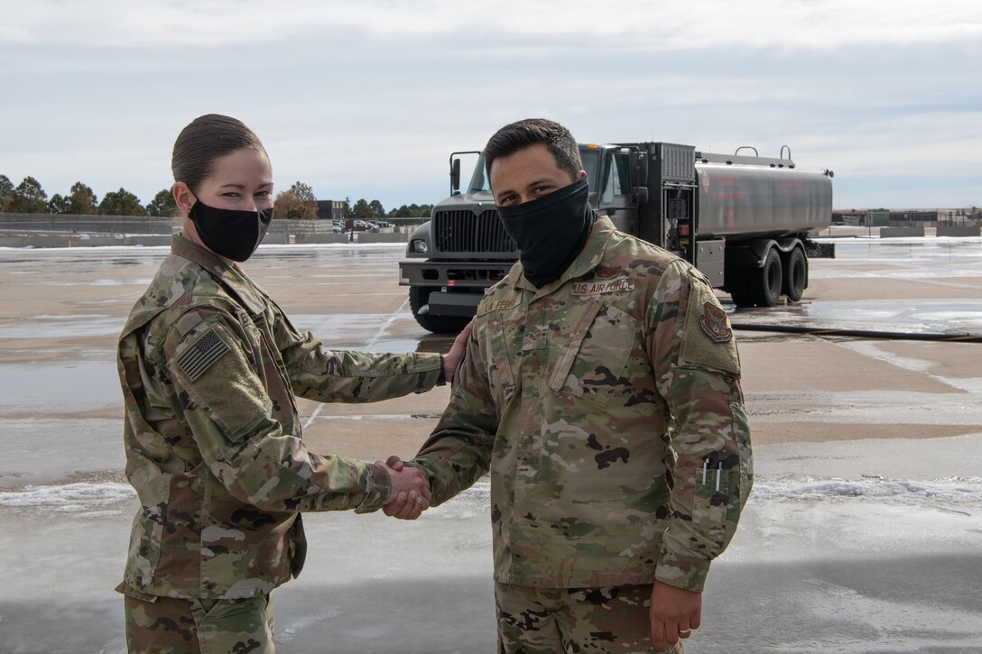 A soldiers shakes the hand of an Airman with a fuel truck in the background on the flight line.
