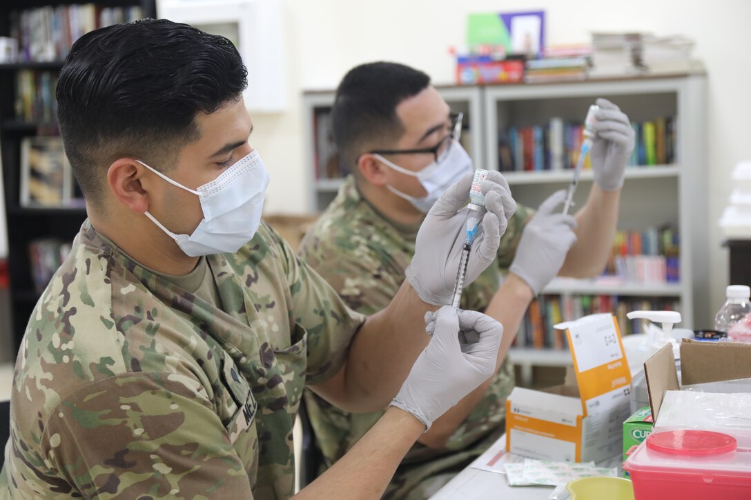 Spc. Michael Meza and Spc. John Cera, healthcare specialists with the 228th Combat Support Hospital, draw doses of the Moderna COVID-19 vaccine from vials at Camp Arifjan, Kuwait, Jan. 18, 2021. Camp Arifjan is utilizing a phased distribution of the vaccine, as specified by the Department of Defense, beginning with medical personnel and first responders.