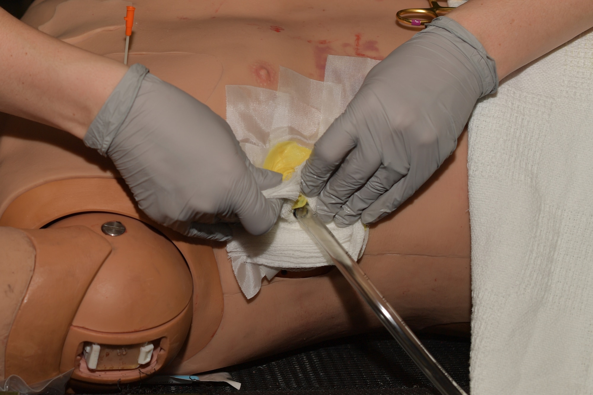 Close-up of Airman's hands working on a simulated medical patient mannequin.
