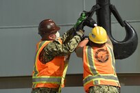 Boatswain�s Mate 2nd Class Sean Hoyle, left and from Morgan Hill, Calif., and Boatswain's Mate 1st Class Carlos Rodriguez, from Phoenix, Ariz. and both deployed with the Navy Expeditionary Logistics capability of Task Force 75, connect a Mark VI patrol boat cradle to the twin crane.