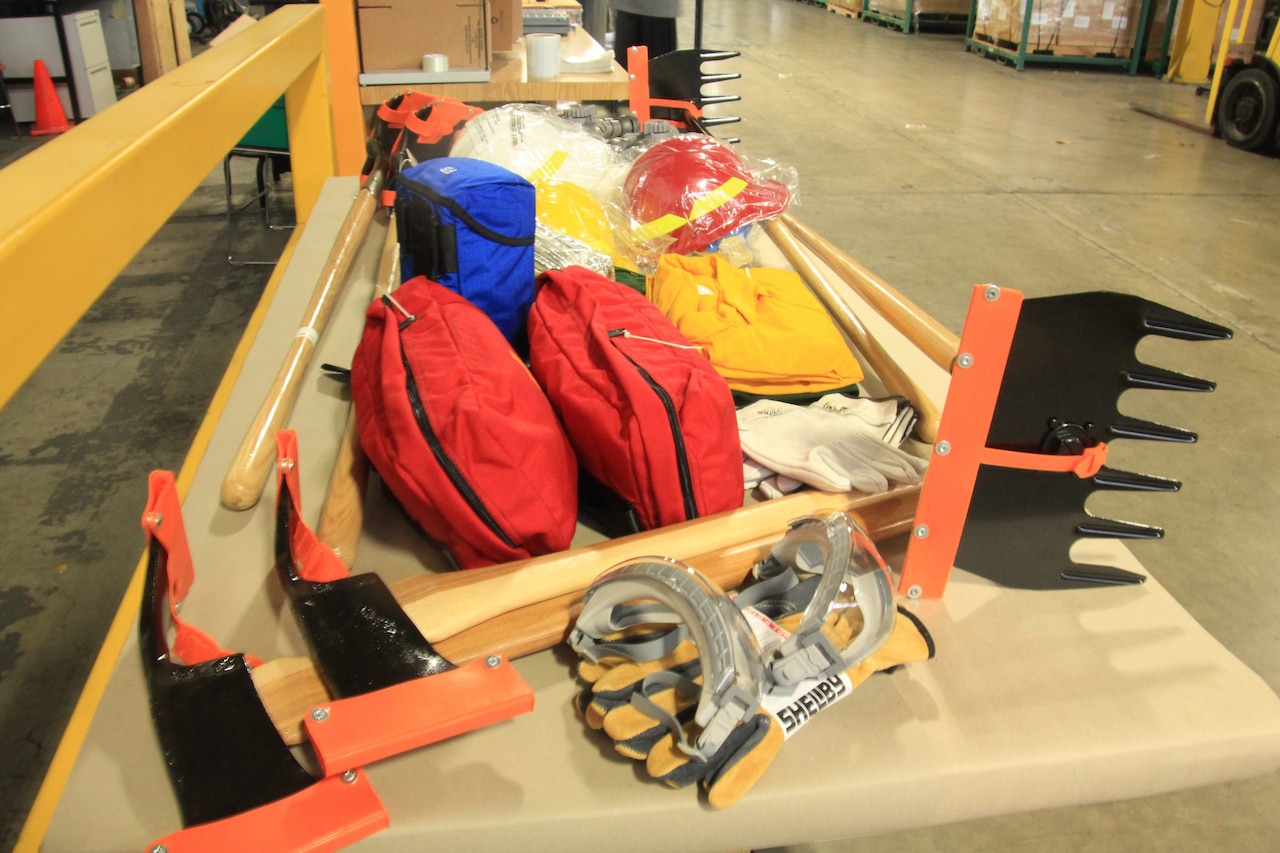 A number of heavy-duty picks, racks, work gloves, helmets, goggles and equipment in nylon bags sit on a table.