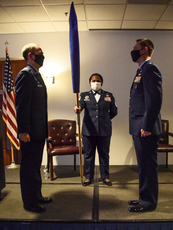 Three service members stand at attention in front of the 355th MDG flag.