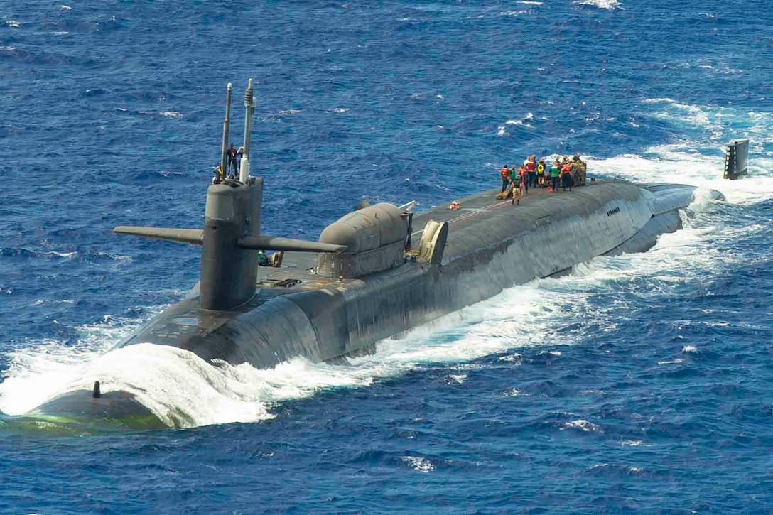 Marines stand on top of a submarine as it travels through waters.