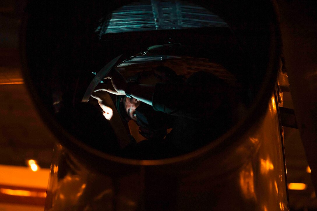 A sailor works inside the cell cavity of an aircraft.