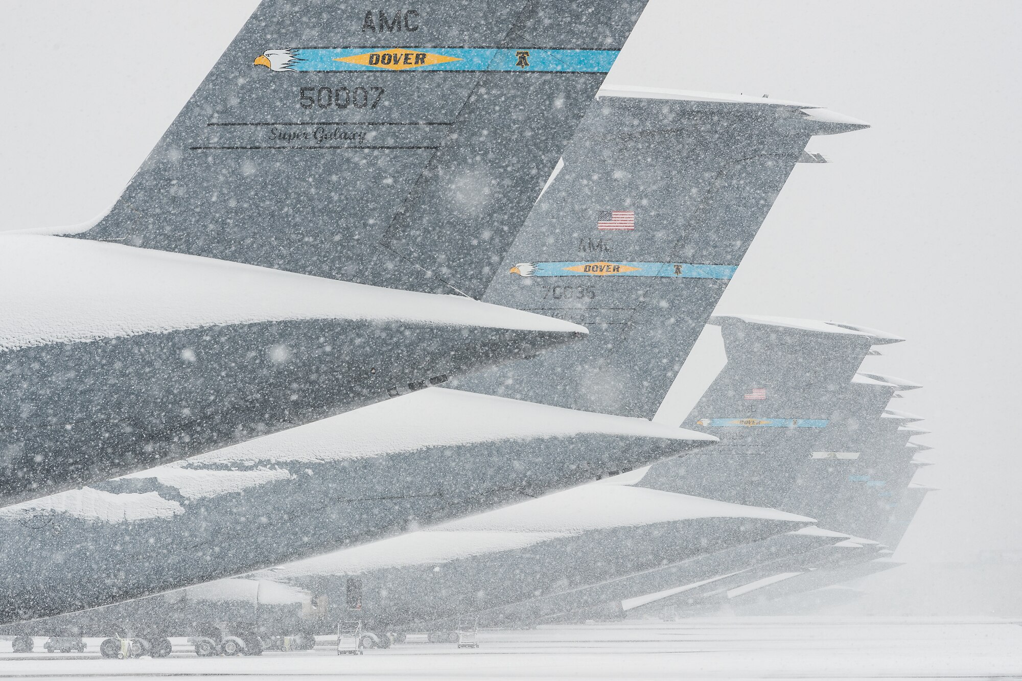 Tails of snow-covered C-5M Super Galaxy aircraft sit on the flight line at Dover Air Force Base, Delaware, Feb. 11, 2021. As Winter Storm Roland produced a wintry mix of precipitation, the base continued normal operations and prepared for additional forecast snowfall. (U.S. Air Force photo by Roland Balik)