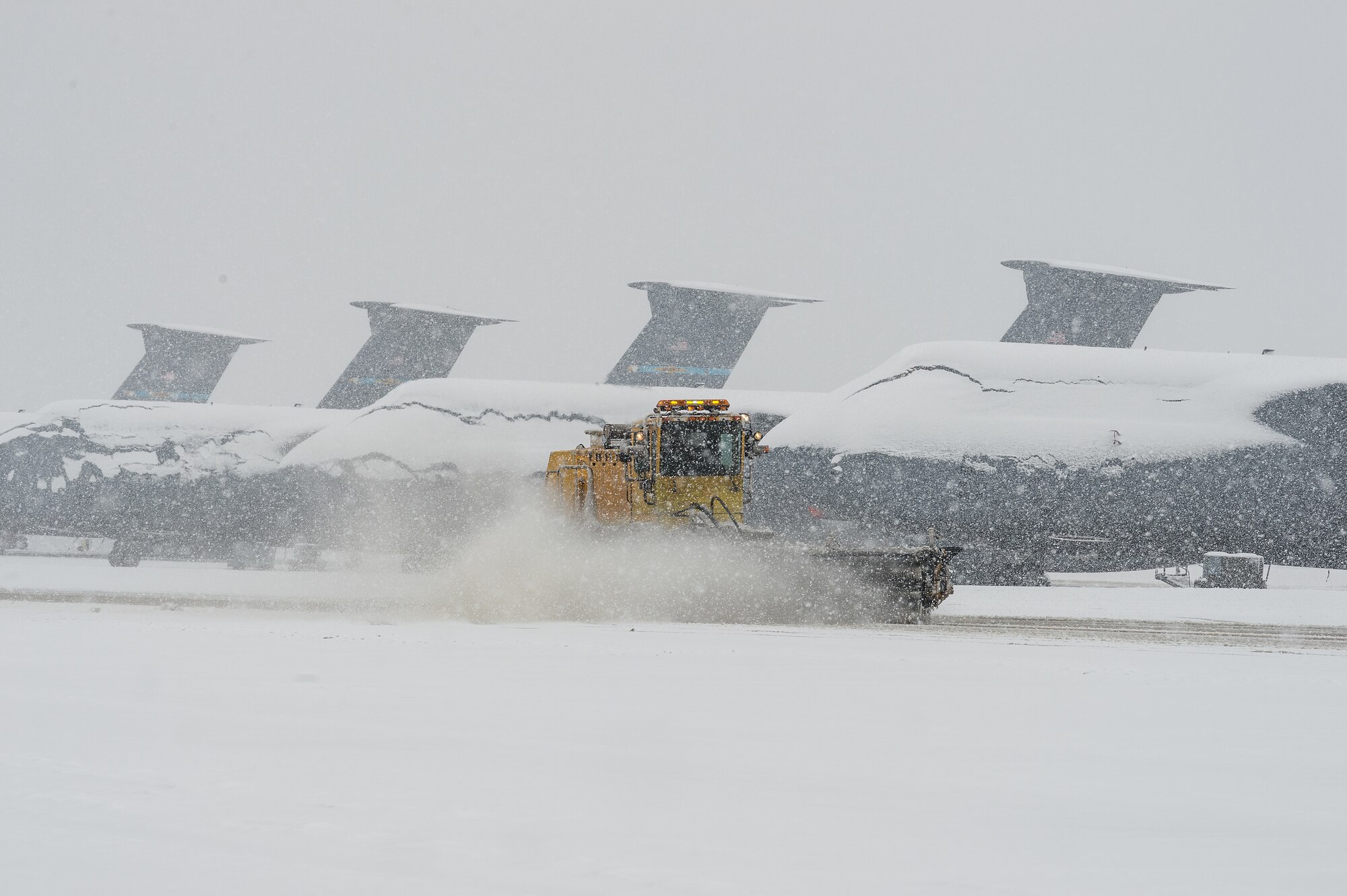 Snow-covered C-5M Super Galaxy aircraft sit on the flight line as a snowplow from the 436th Civil Engineer Squadron clears snow at Dover Air Force Base, Delaware, Feb. 11, 2021. As Winter Storm Roland produced a wintry mix of precipitation, the base continued normal operations and prepared for additional forecast snowfall. (U.S. Air Force photo by Roland Balik)