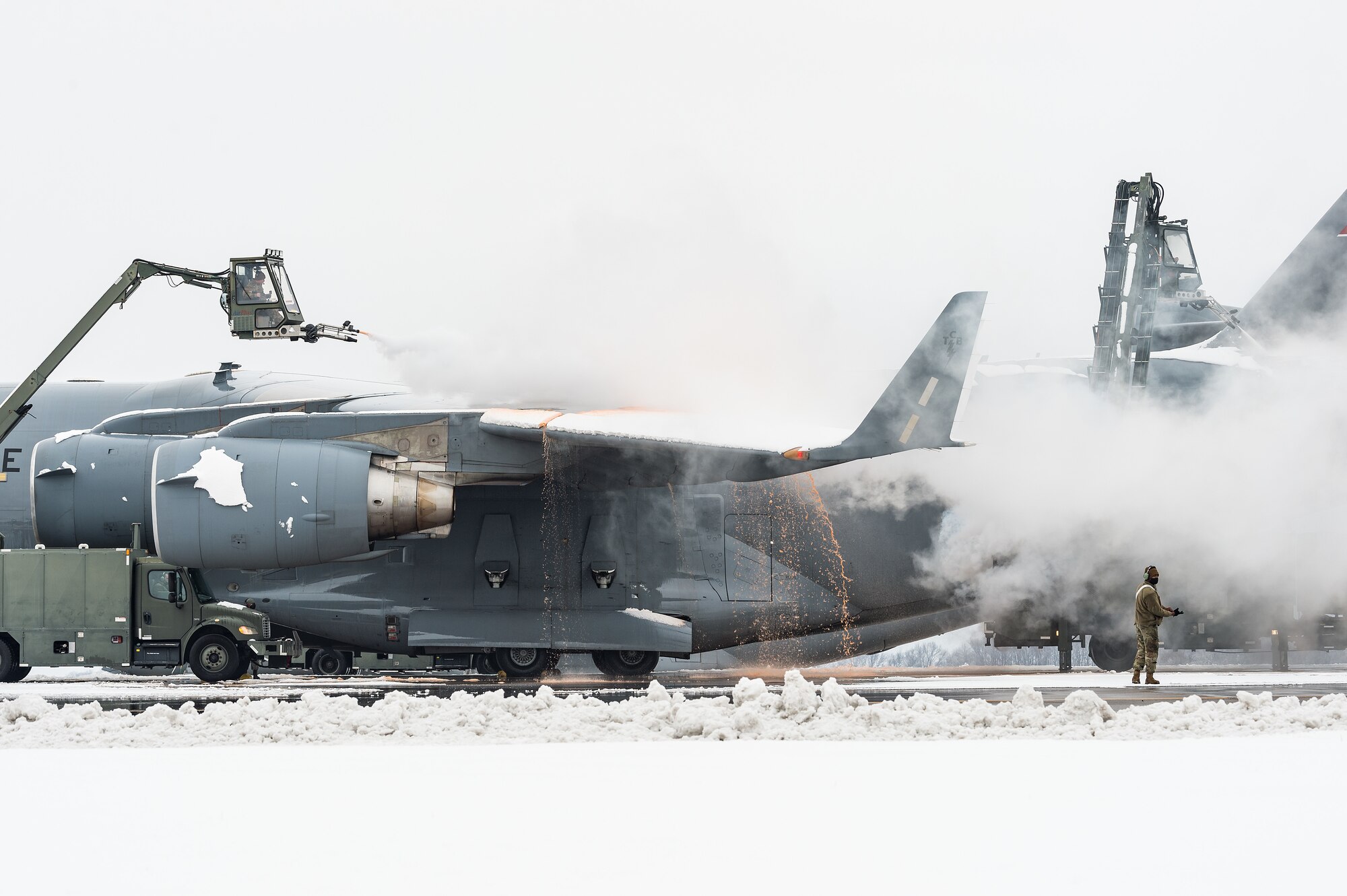 De-icing vehicles remove snow from the left wing and aft fuselage areas of a transient Tennessee Air National Guard C-17 Globemaster III prior to departing Dover Air Force Base, Delaware, Feb. 11, 2021. As Winter Storm Roland produced a wintry mix of precipitation, the base continued normal operations and prepared for additional forecast snowfall. (U.S. Air Force photo by Roland Balik)