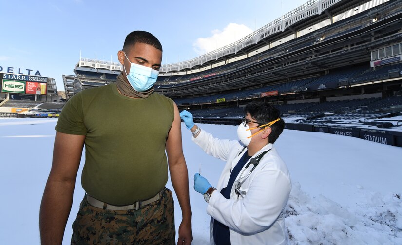 A doctor prepares to give a shot to a Marine at a stadium.