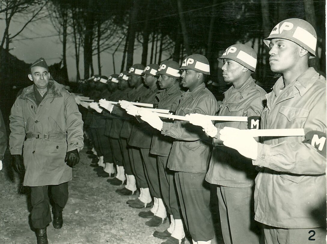 Service members stand in a line as another service member walks by them.