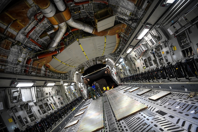 Airmen stand inside the cargo bay of an aircraft.