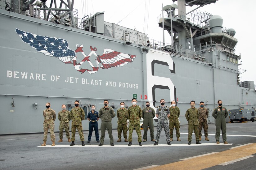 U.S., Australian and Japanese service members stand on a ship's deck.