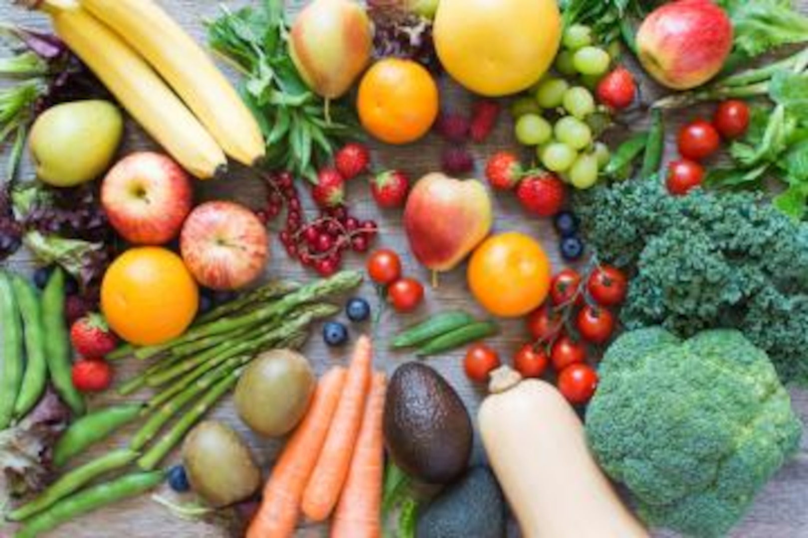  A wooden table covered with fresh fruits and vegetables, including apples, bananas, grapes, oranges, carrots, spinach, and broccoli.