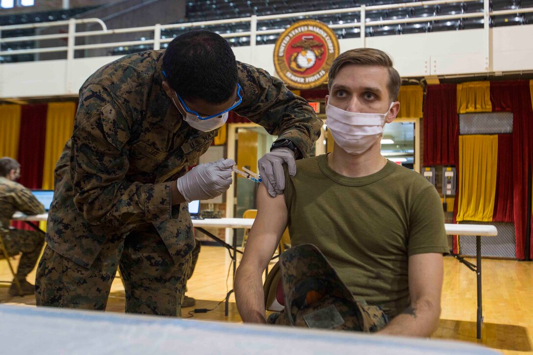 A Marine gives an injection to another Marine.