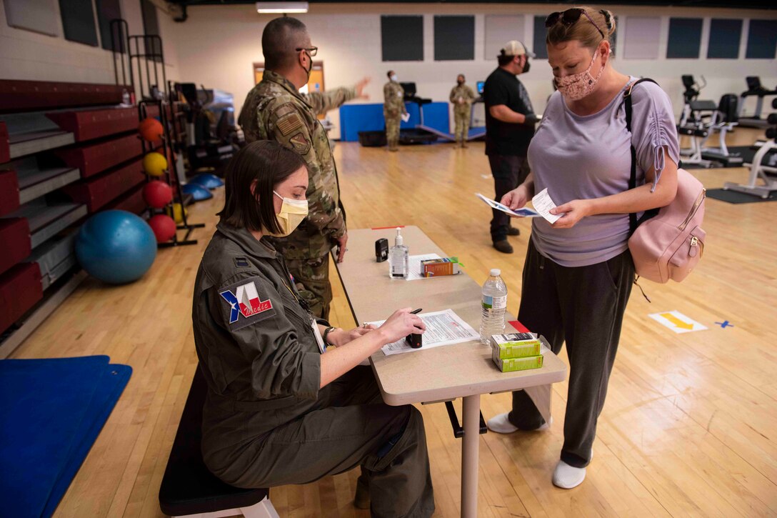 An airman sits at a table as a woman approaches; others seen in the background.