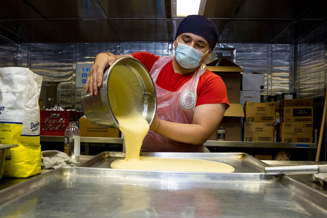 A sailor pours cake batter onto a baking pan.