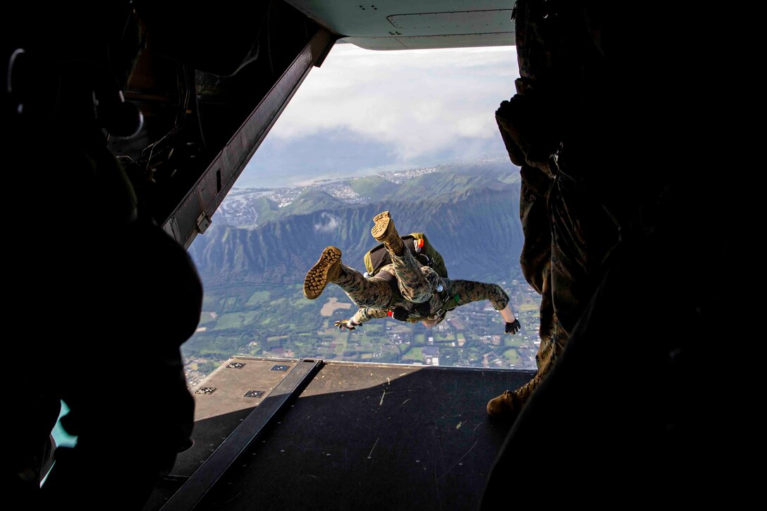 A Marine jumps out the back of an aircraft; mountains can be seen in the background.