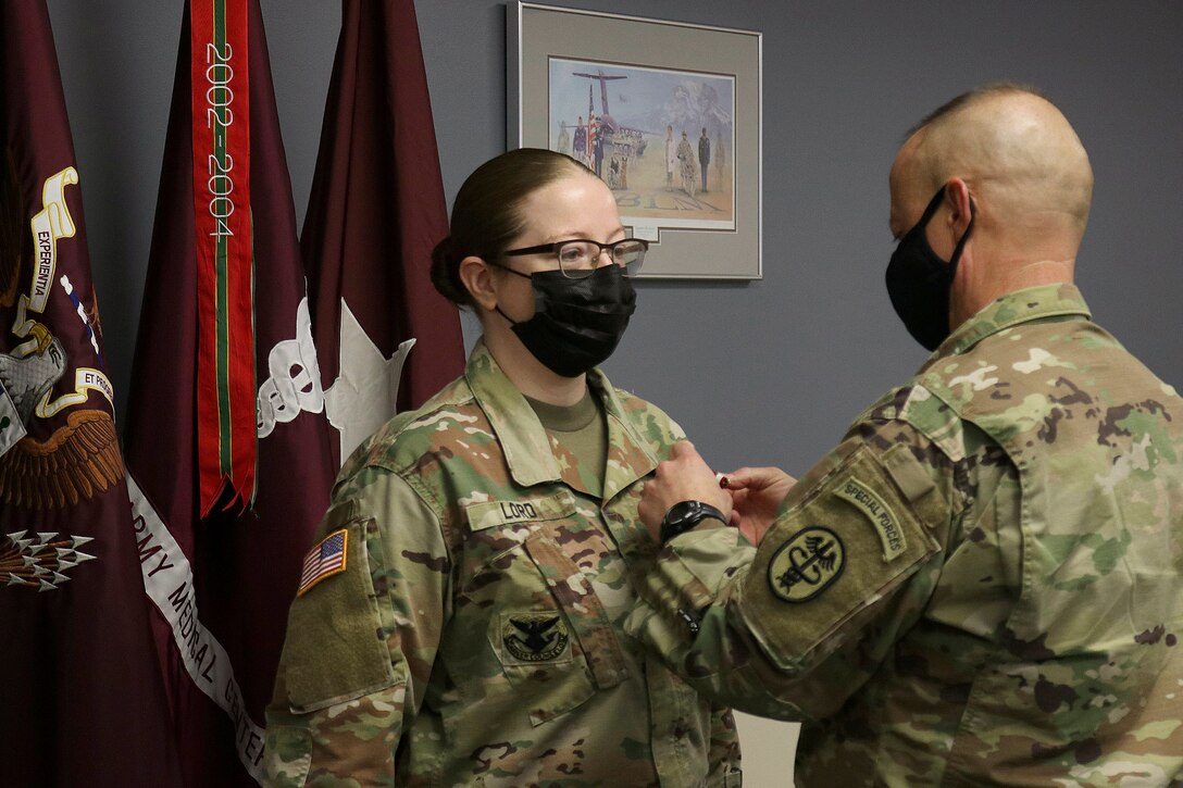 A soldier puts a medal on a fellow soldier’s collar.