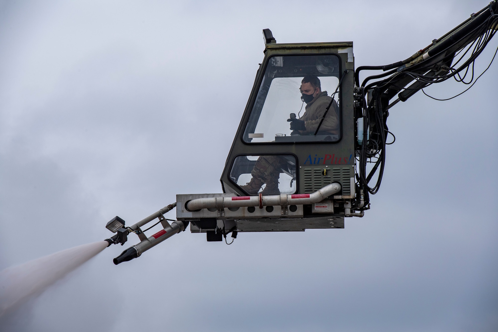 A crew chief de-ices a C-130 on the flightline.
