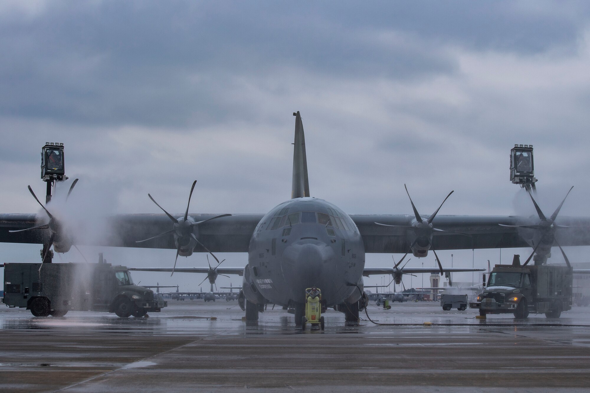 two de-icing trucks de-ice a C-130.