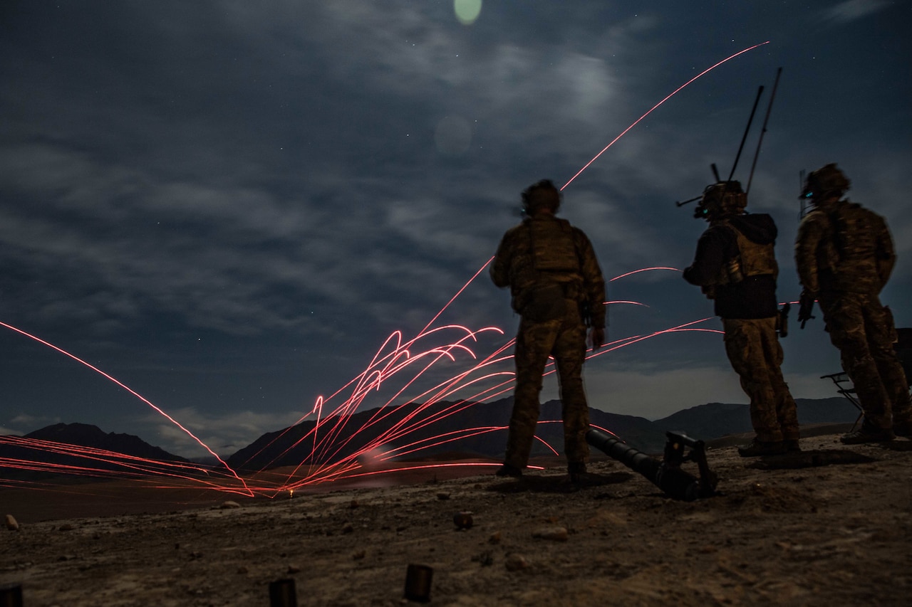 Tracers skim through the sky as service members look on in Afghanistan.