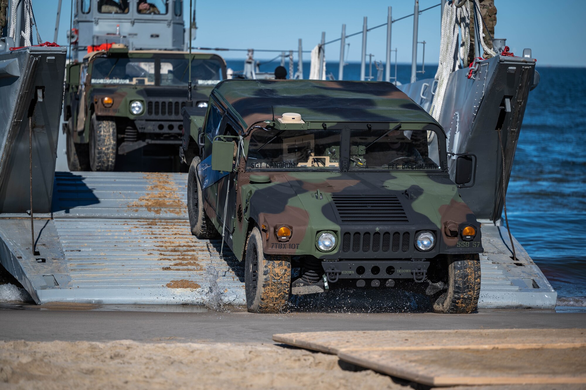 A Humvee drives off a boat on the shore.