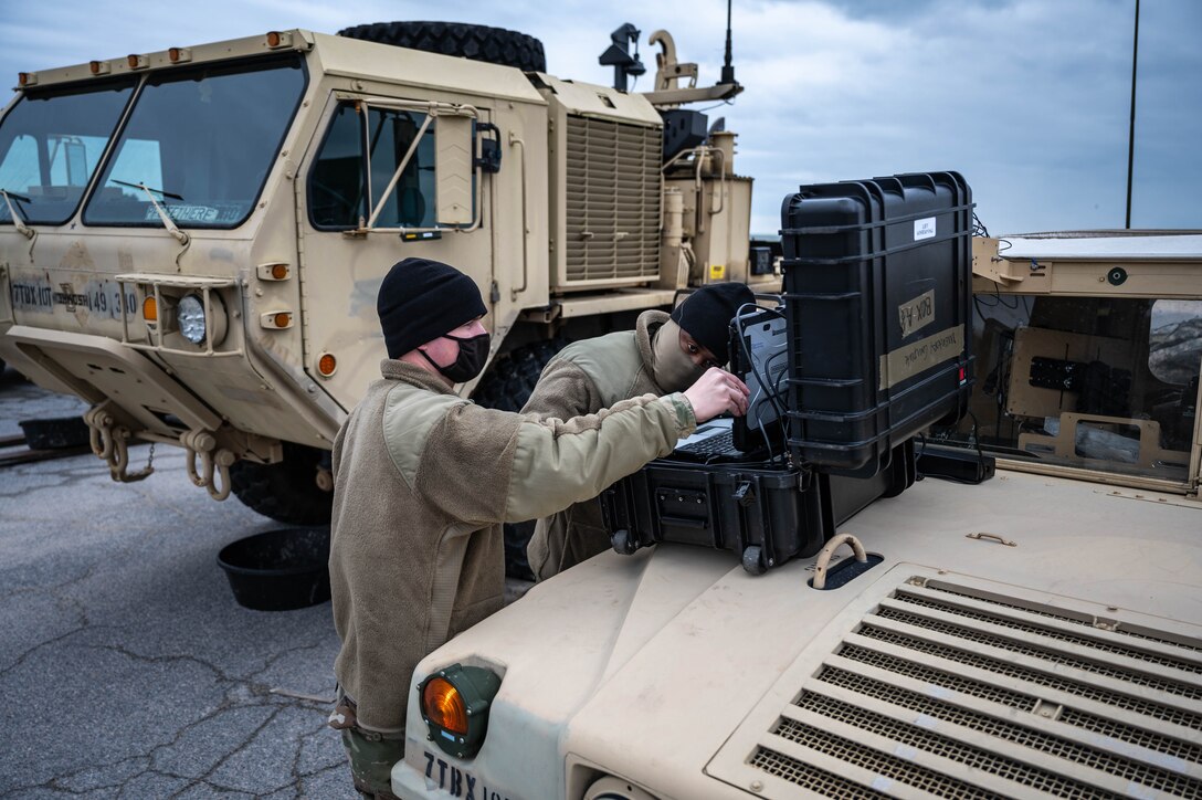 Two Soldiers check an inventory computer on the hood of a Humvee.