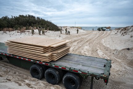 A flatbed truck holds boards for soldiers to make a boardwalk on the beach.
