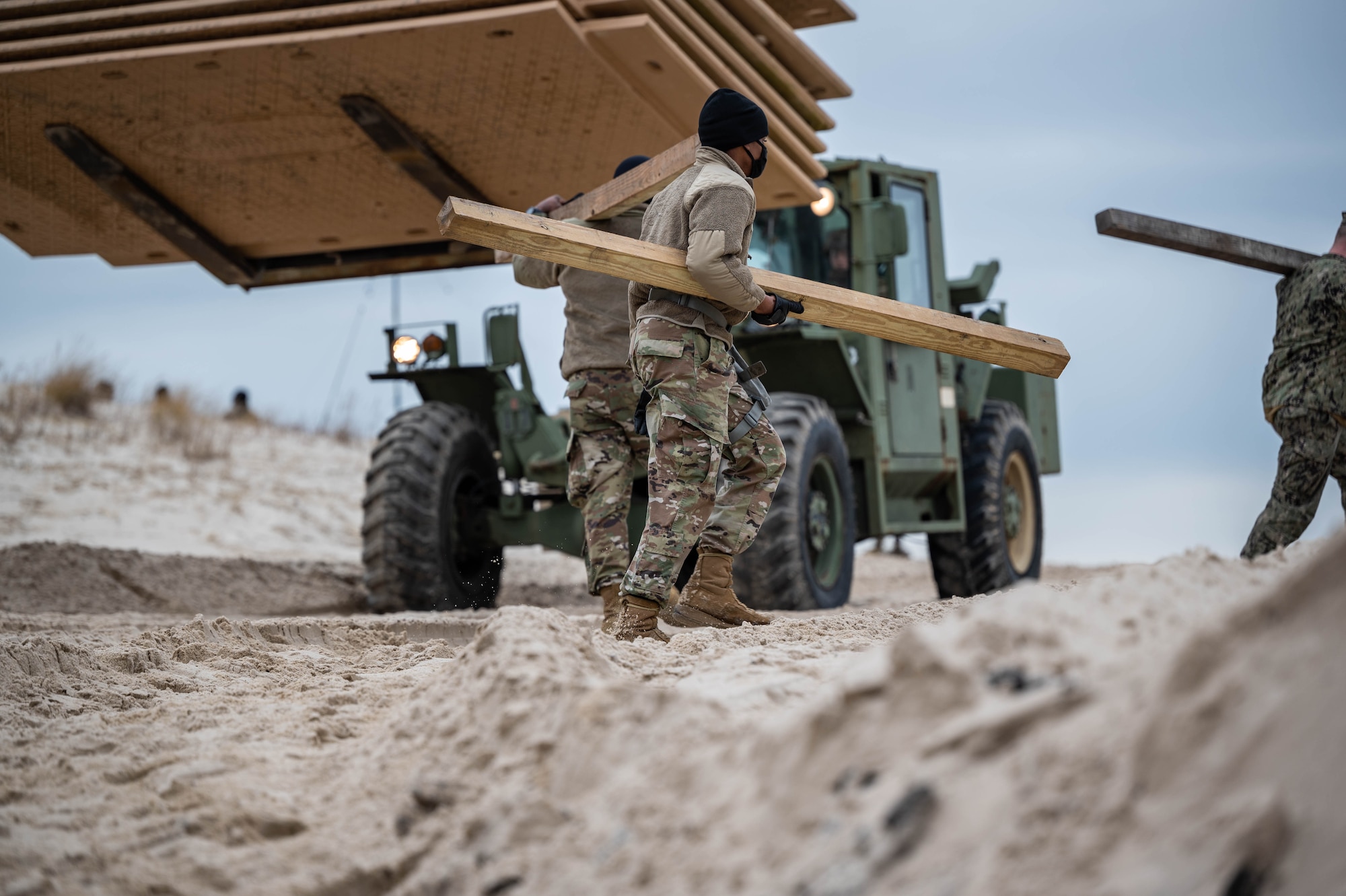 Soldiers carry boards for a boardwalk at the beach.