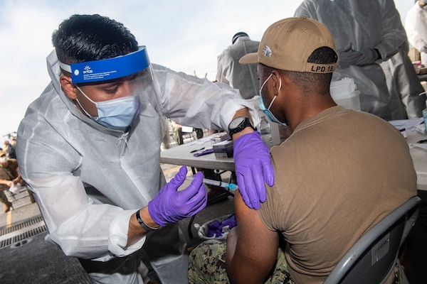 Hospital Corpsman 1st Class Javier Flores gives a COVID-19 vaccination to Retail Services Specialist Seaman Jordan Davis aboard amphibious transport dock ship USS New Orleans (LPD 18).