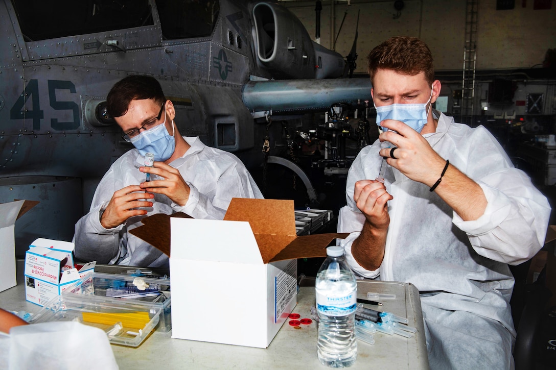 Navy seaman wearing face masks prepare COVID-19 vaccination shots.