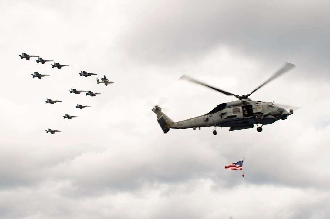 Aircraft fly in formation near a helicopter displaying an American flag.