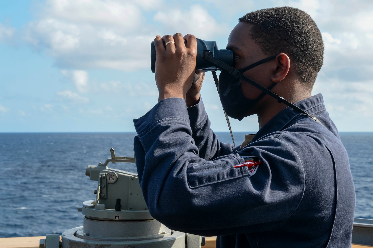 U.S. Navy Ensign Ryan Simpson, from Baltimore, looks through a pair of binoculars on the bridge wing as the guided-missile destroyer USS Russell (DDG 59) conducts routine underway operations.