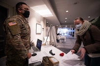 Army Spc. Anthony Moreno walks Navy Lt. Courtney Corcoran, assigned to Naval Medical Center Camp Lejeune, through the check-in process at a local New Jersey hotel, Feb. 11, 2021. Corcoran is part of a team of service members traveling to New Jersey in support of COVID-19 vaccine operations.
