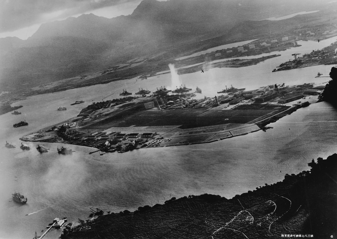 Photograph taken from Japanese plane during torpedo attack on ships moored on both sides of Ford Island; view looks about east, with supply depot, submarine base, and fuel tank farm in right center distance; torpedo has just hit USS West Virginia on far side of Ford Island (center); other battleships moored nearby are (from left): USS Nevada, USS Arizona, USS Tennessee (inboard of West Virginia), USS Oklahoma (torpedoed and
listing) alongside USS Maryland, and USS California; on near side of Ford Island (left), are USS Detroit and USS Raleigh, USS Utah and USS Tangier; Raleigh and Utah have been torpedoed, and Utah is listing sharply to port; Japanese planes are visible in right center (over Ford Island) and over Navy Yard at right, Pearl Harbor, December 7, 1941 (Navy Ministry, Empire
of Japan/U.S. Naval History and Heritage Command)