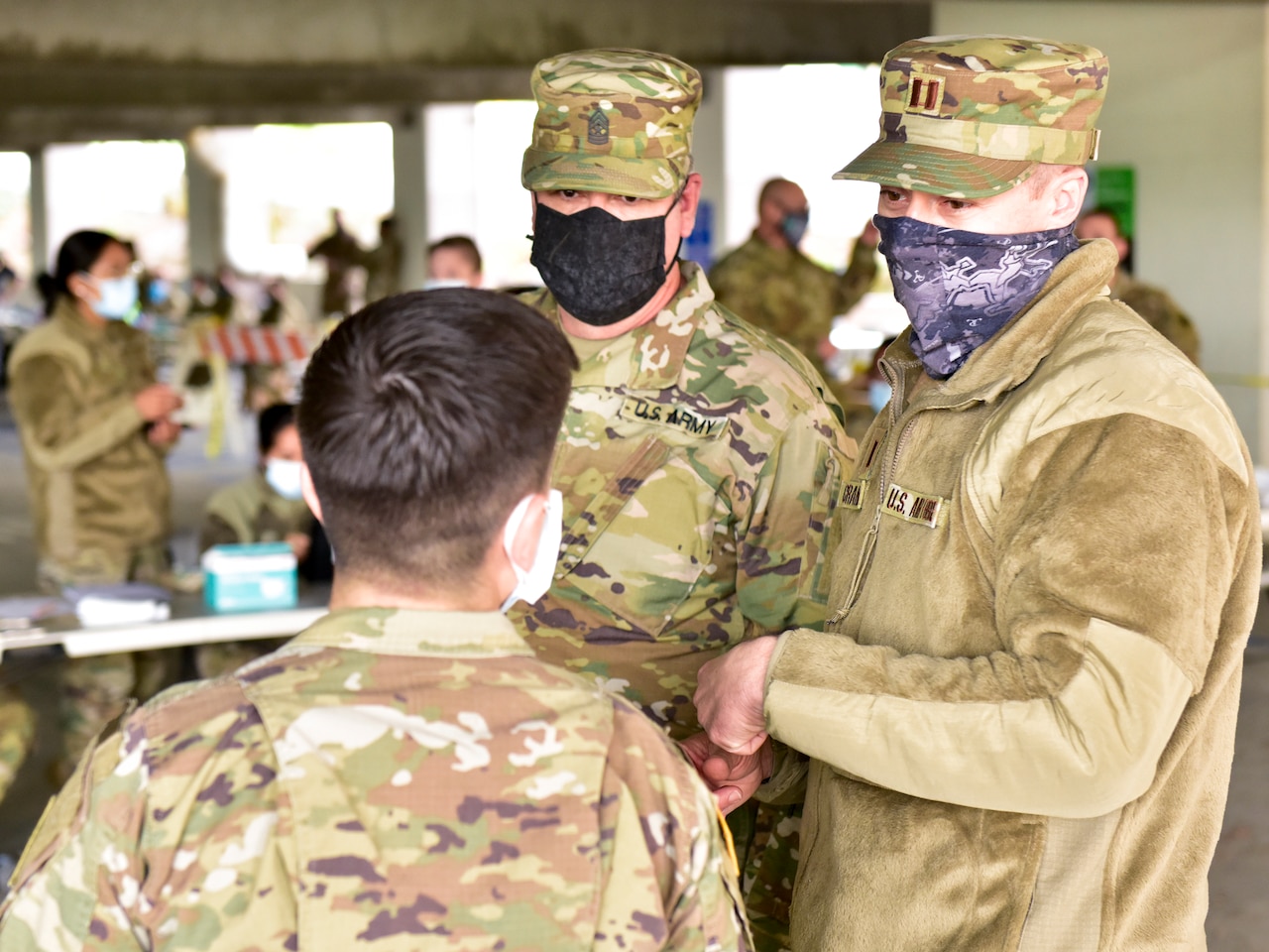 Two men in military uniforms talk with another man wearing a military uniform.