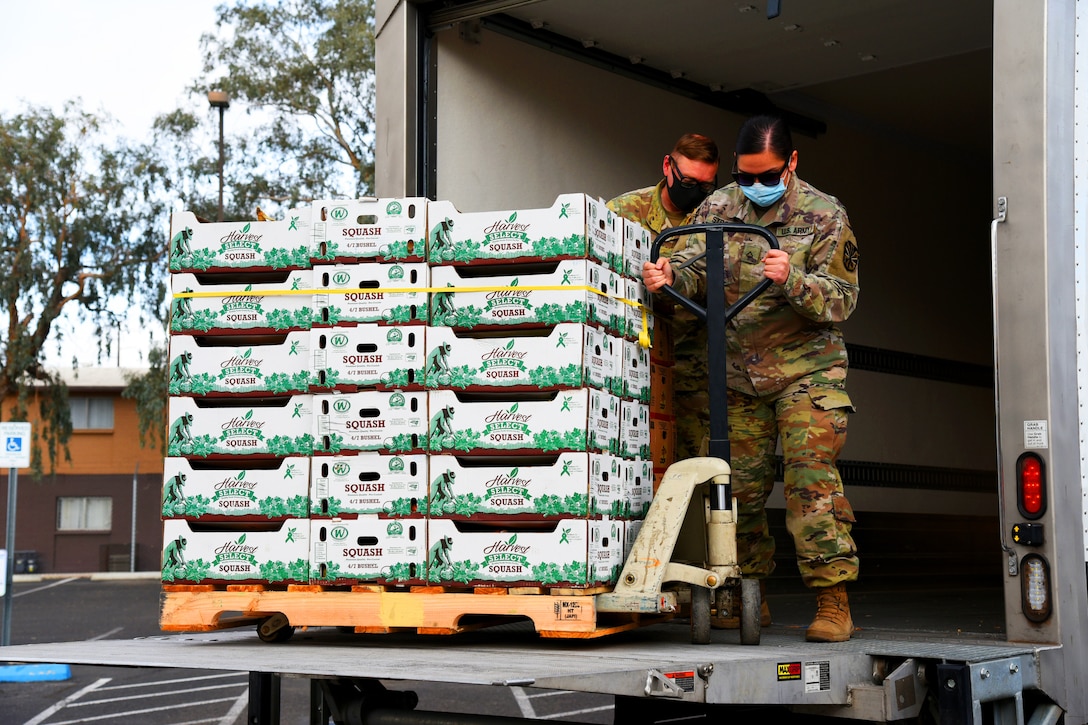 Two soldiers wearing  face masks help unload boxes of produce for distribution.