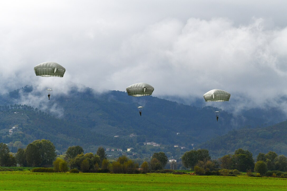Three paratroopers descend toward a field.