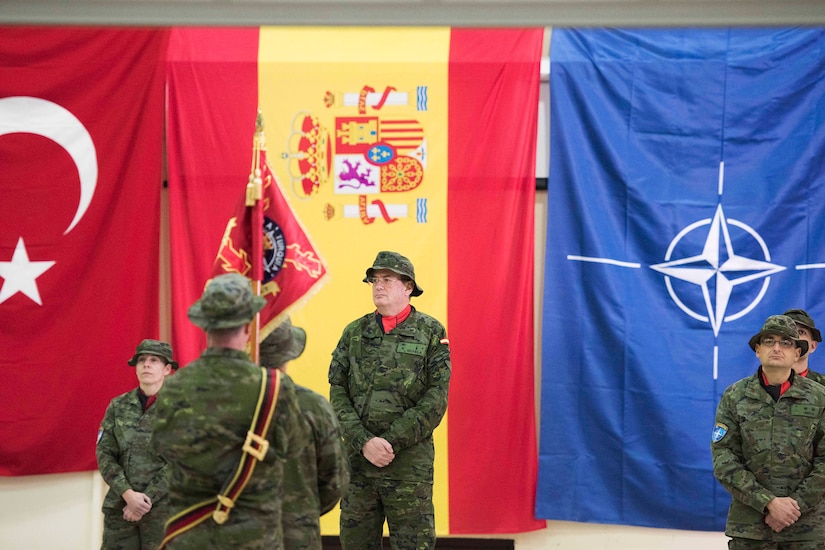 Five soldiers stand in front of flags.