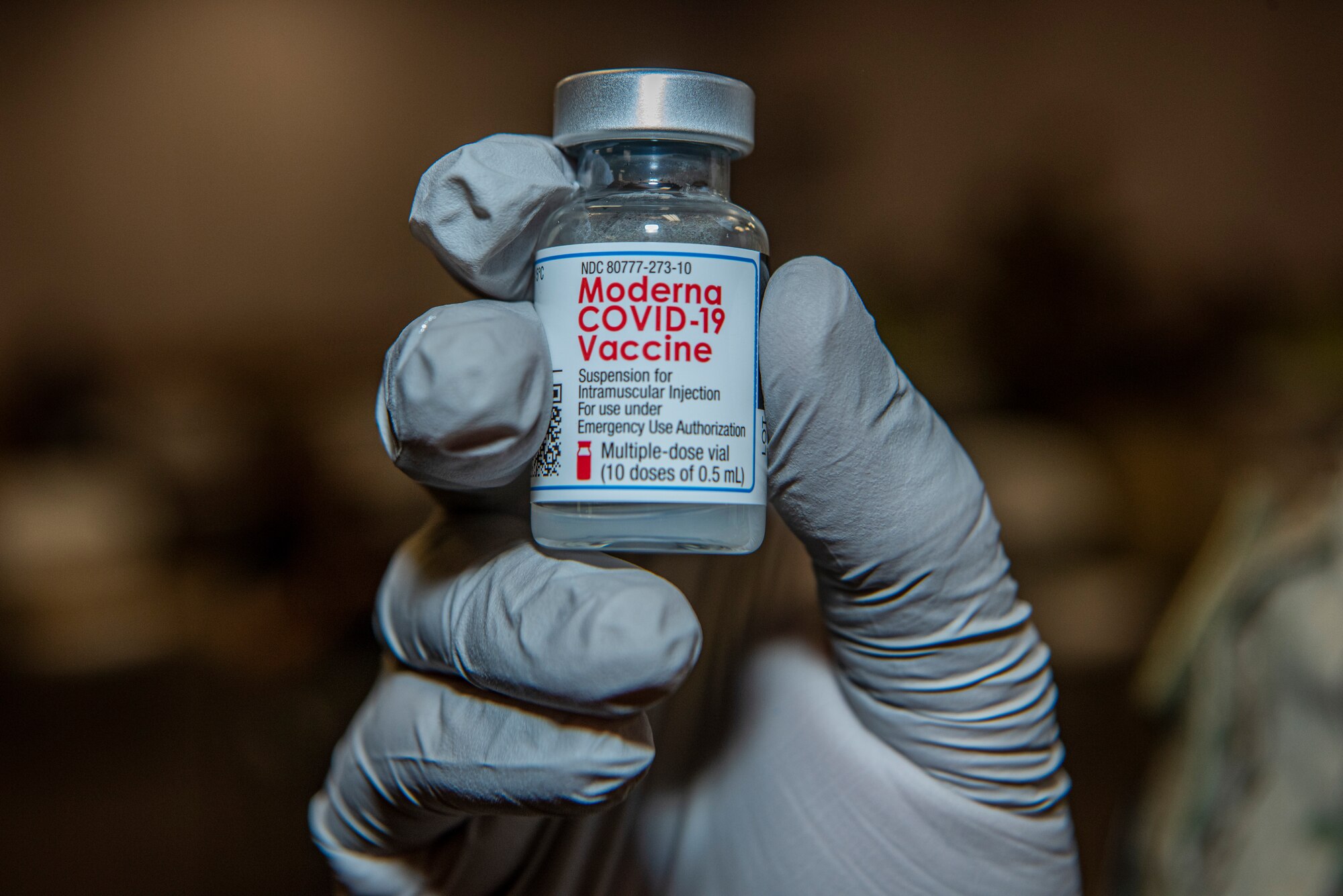 hand with glove holding vile of COVID-19 vaccine