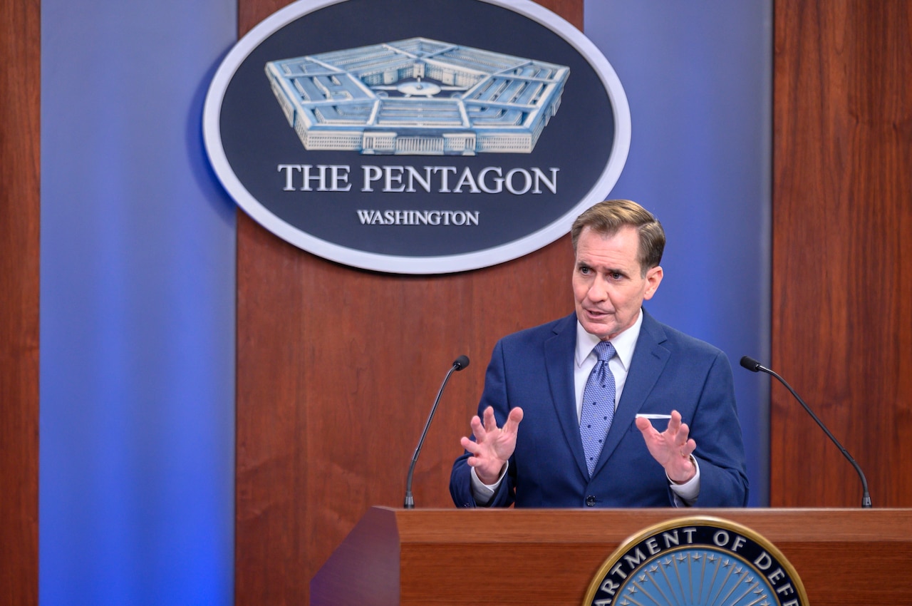 A man at a lectern with two microphones gestures. The sign behind him indicates that he is at the Pentagon.