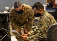 U.S. Army Maj. Ashish Patel, the chief of current operations in the Joint Operations Center at Task Force Northeast (TF-NE), right, and Air Force Lt. Col. Kirk Deitrich, the J35 future operations division chief, discuss Federal COVID-19 response operations at TF-NE headquarters on Fort Eustis, Va., during distributed operations.
