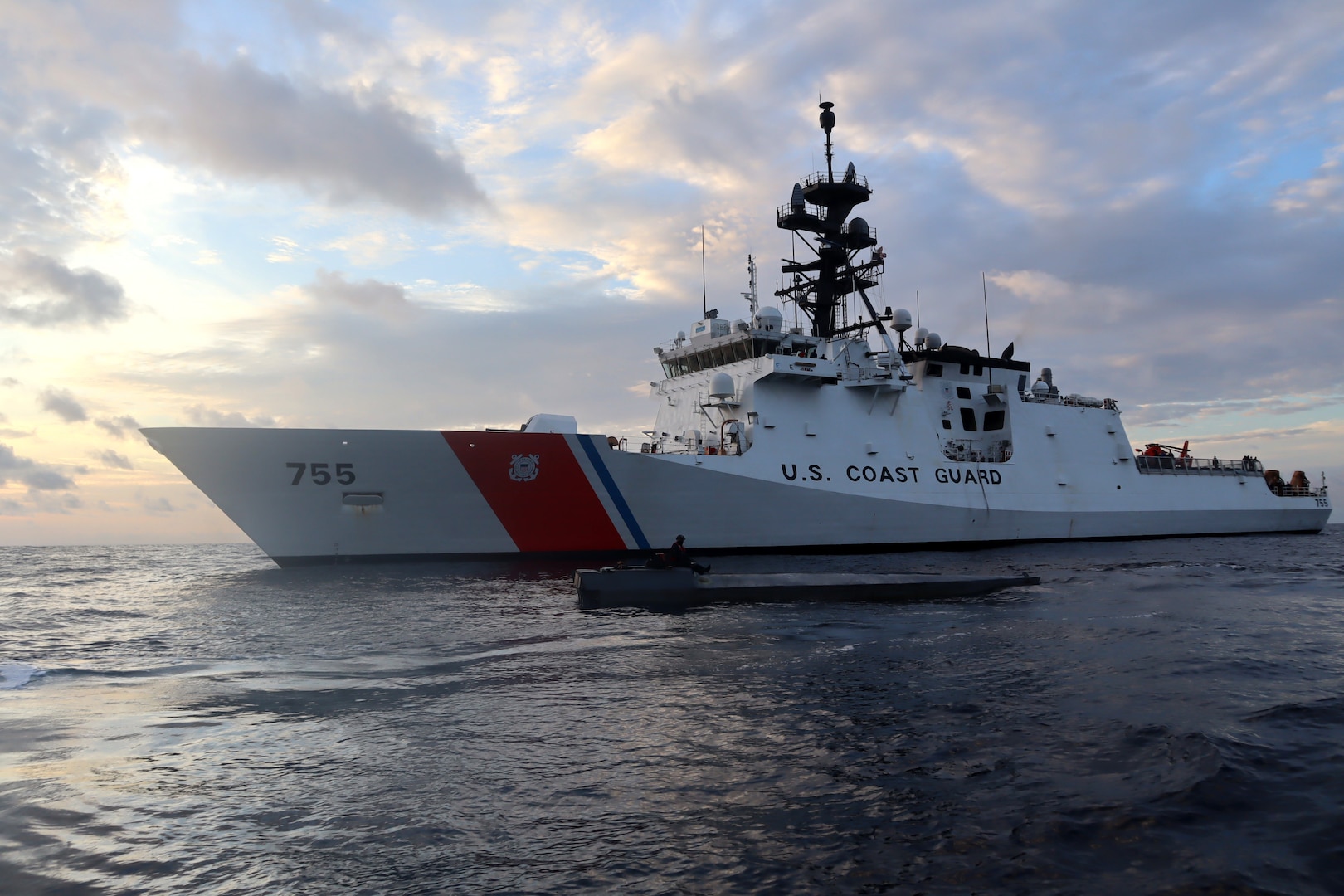 Coast Guard Cutter Munro (WMSL 755) boarding team member sits atop an interdicted low-profile vessel in the Eastern Pacific Ocean after crews seized 3,439 pounds of cocaine from the LPV, Jan. 27, 2021.