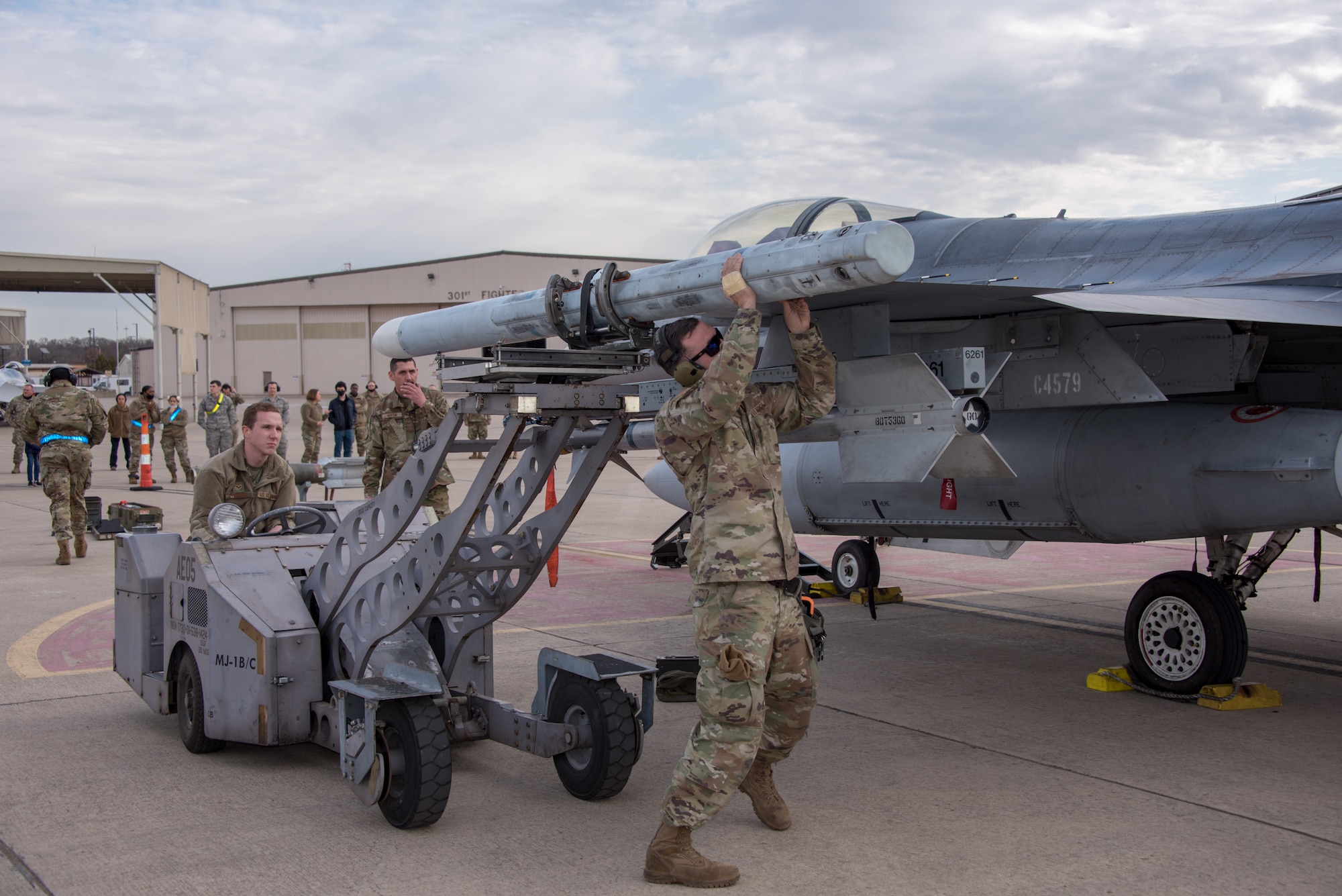 (Right) Tech. Sgt. Dalton King, 301st Fighter Wing Aircraft Maintenance Squadron load crew lead, lifts an AIM-120 missile, preparing to secure it to the 301st Fighter Wing’s F-16, as (left) Senior Airman Jaymes Fincher positions the weapons loader during a weapons load competition at U.S. Naval Air Station Joint Reserve Base Fort Worth, Texas on February 5, 2021. The competition consists of four, three-person AMXS load crews quickly uploading weapons on 301st Fighter Wing F-16s, while maintaining a strict attention to detail, with hopes of winning load crew of the year. (U.S. Air Force photo by Senior Airman William Downs)