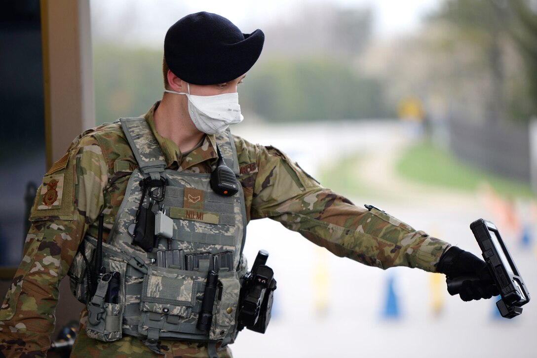 Airman 1st Class Matthew Neimi of the 88th Security Forces Squadron scans the ID card of a retiree at Wright-Patterson Air Force Base last March. Under new Defense Department guidelines, masks and face coverings must be worn upon installation entry but lowered briefly for identification purposes. (U.S. Air Force photo by Ty Greenlees)