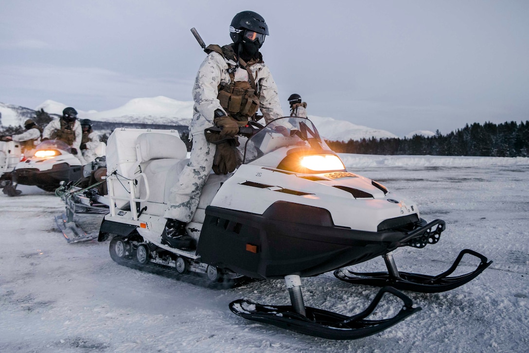 A Marine operates a snowmobile; others are seen behind.