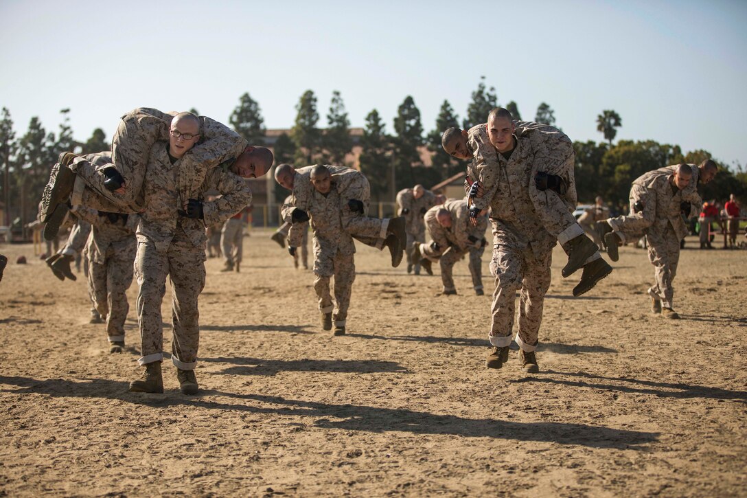 Marines walk in a line while carrying fellow Marines over their shoulders.