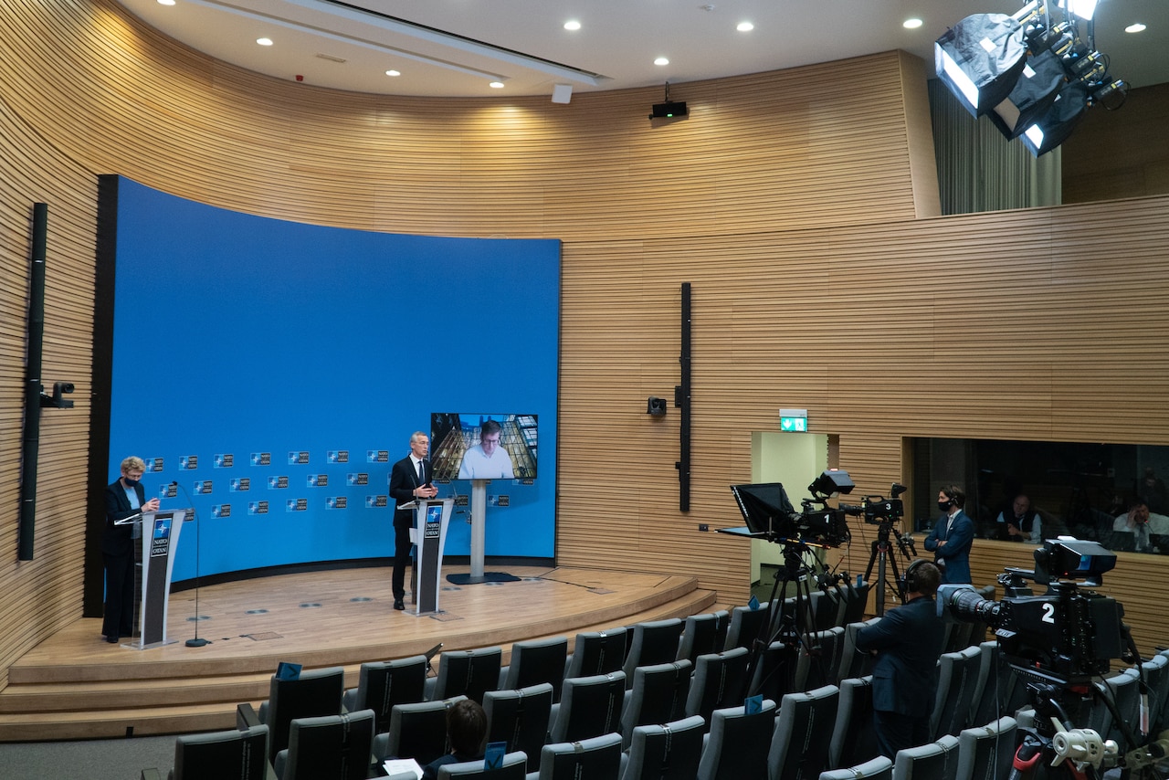 Man in nearly-empty auditorium speaks to TV cameras.