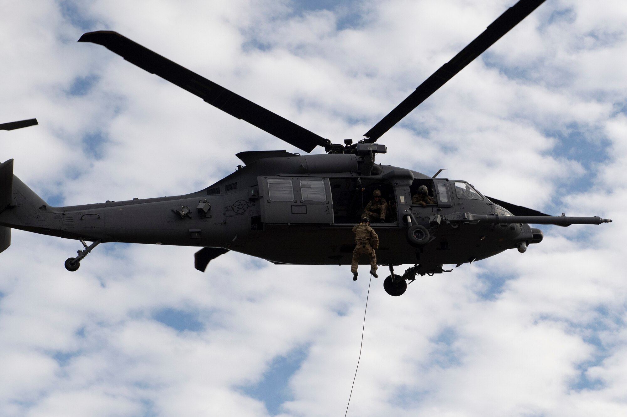 A rescue airman descends from a helicopter from a rappel line.