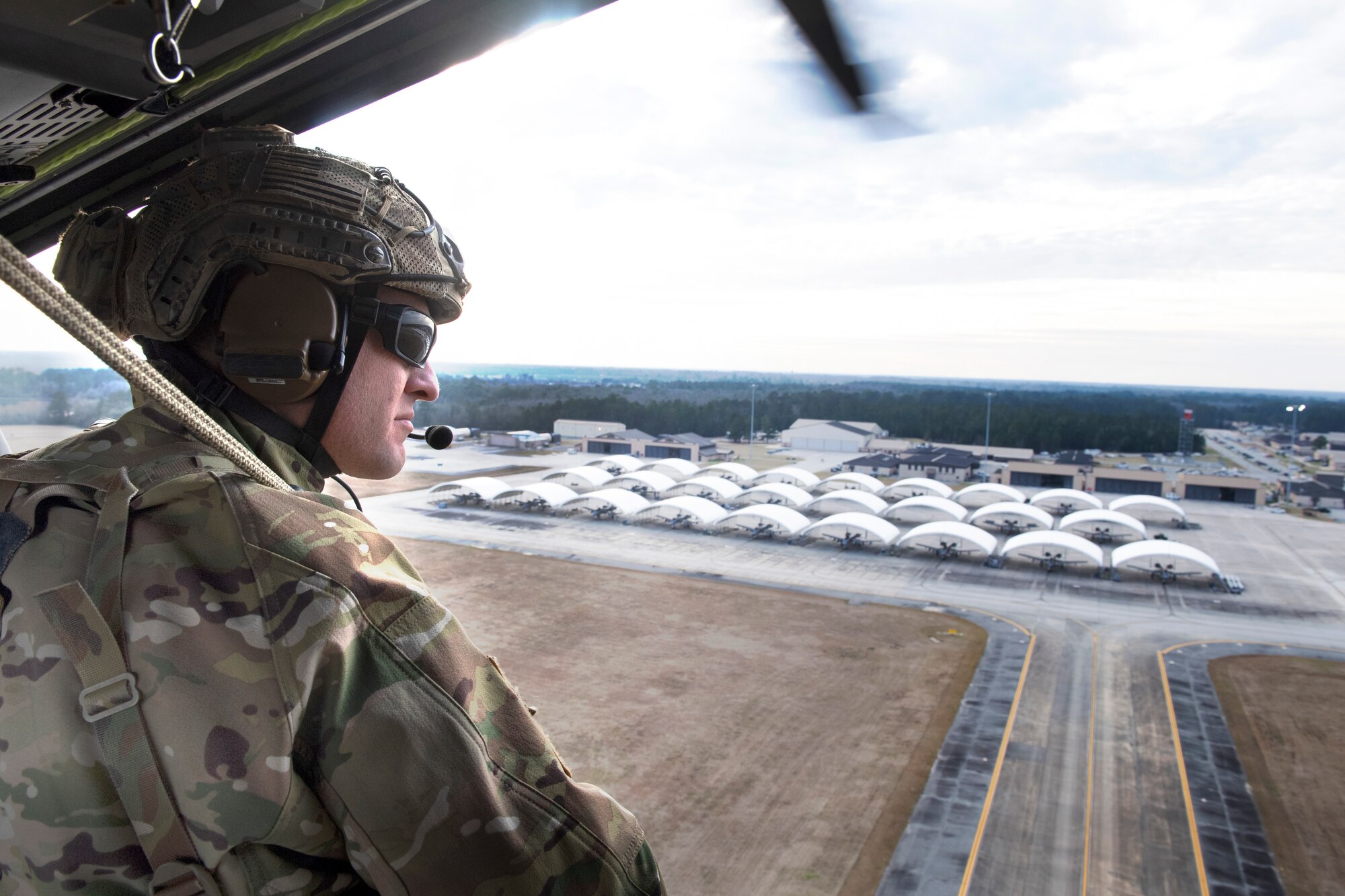 A photo of a rescue airman looking over the flightline from the side of a helicopter.